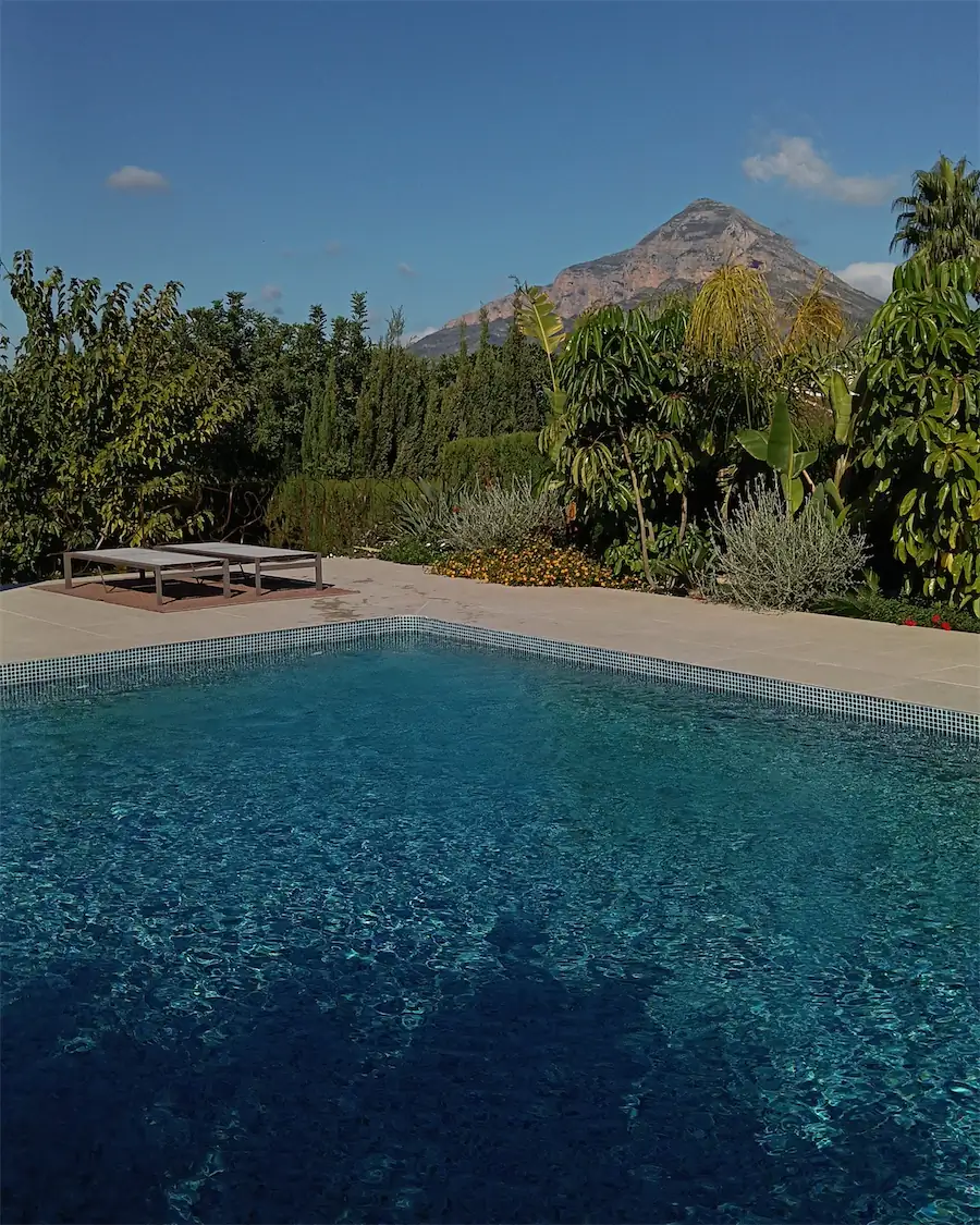 Piscina con tumbonas y un jardín tropical delante